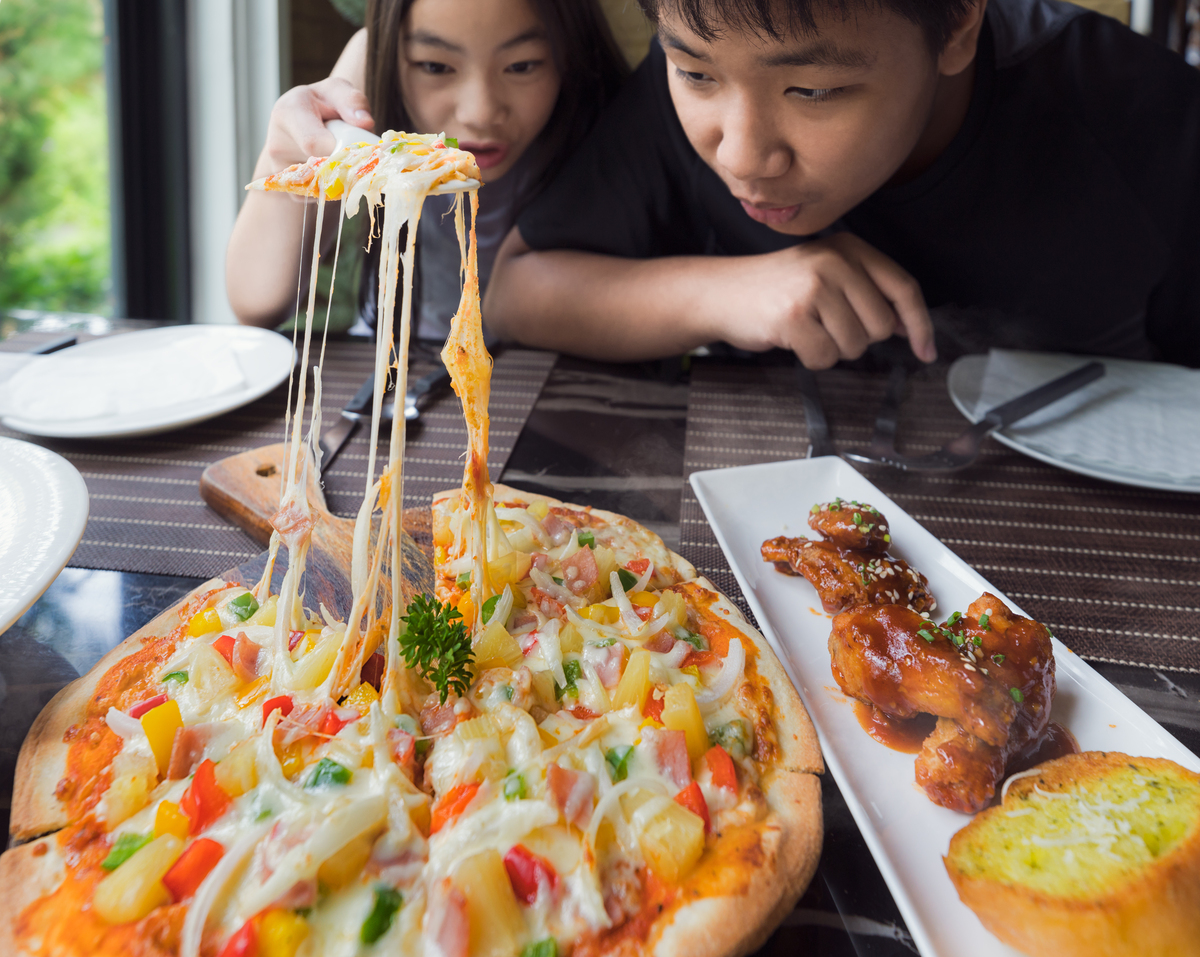 Two children eating pizza, cutting it in slices