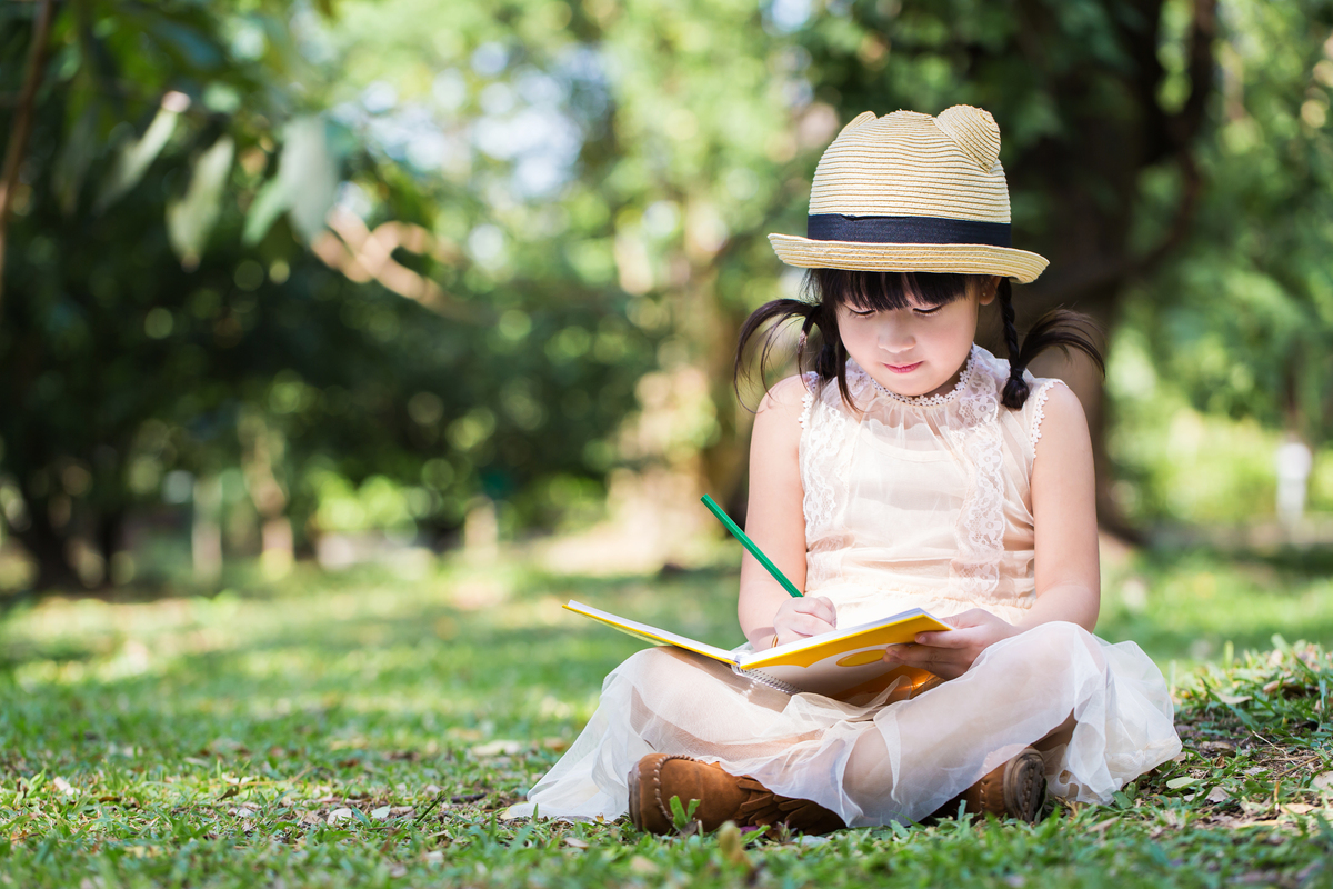 Math and outdoor learning girl sitting on grass with a book reading